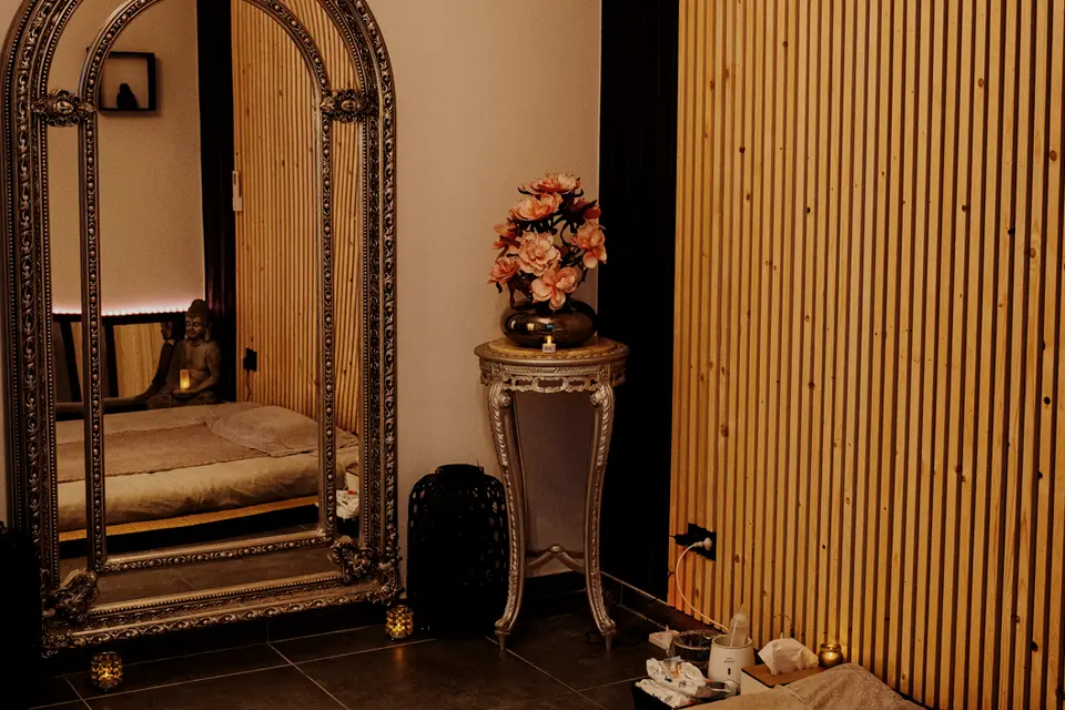 Cabine de massage aux murs en lattes de bois, grand miroir baroque argenté et futon au sol