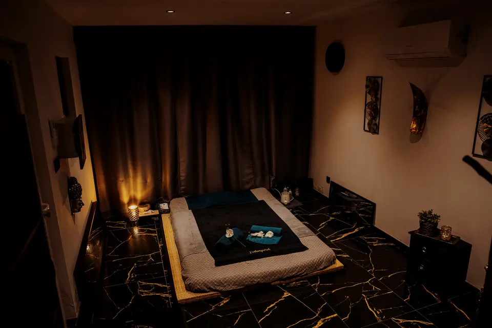 Cabine de massage au sol de marbre noir veiné d’or, futon, rideaux sombres et bougies