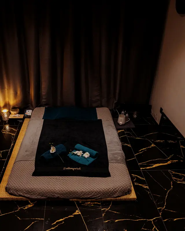 Cabine de massage à la lueur des bougies : futon, linge noir, sol de marbre veiné d’or