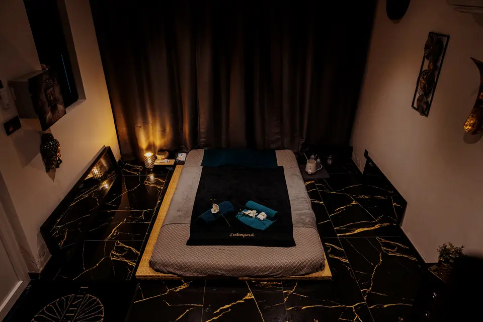Cabine de massage à la lueur des bougies : futon, linge noir, sol de marbre veiné d’or
