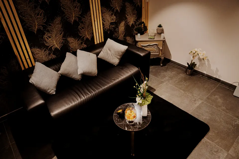 Le salon : canapé de cuir noir, papier peint à plumes dorées, orchidée
